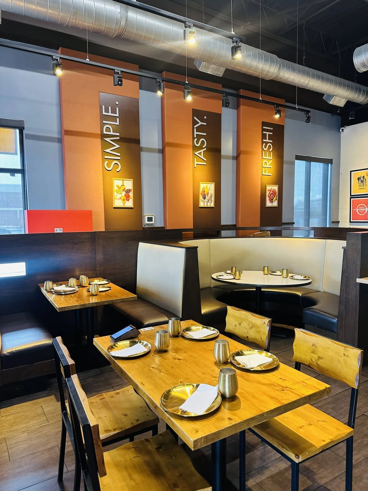 The booth room at Indian Curry, gold place settings laid on every table under SIMPLE. TASTY. FRESH! banners.