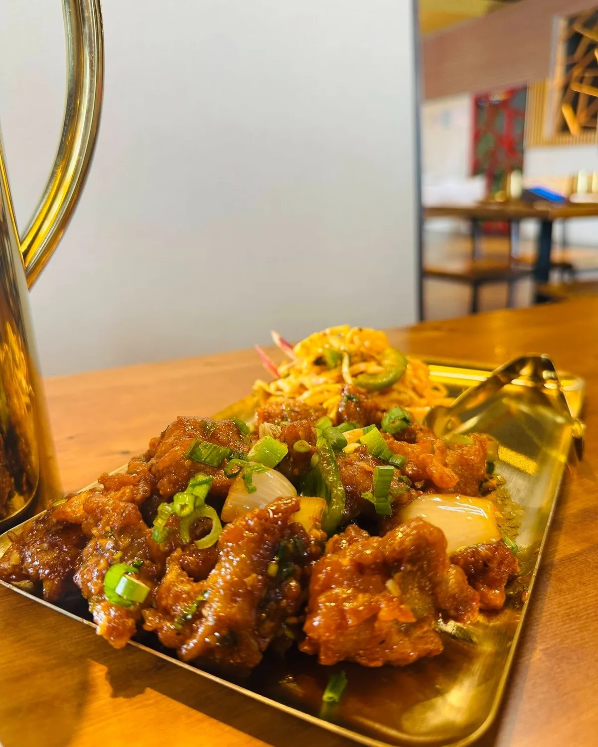 Chicken chili on a gold tray with spring onion, a brass pitcher behind.