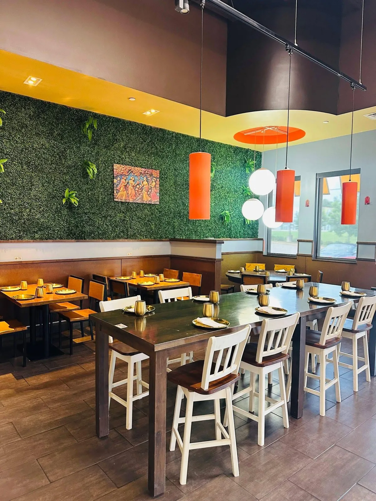 The green hedge wall at Indian Curry with a painted mural, orange cylinder pendants over a long table.