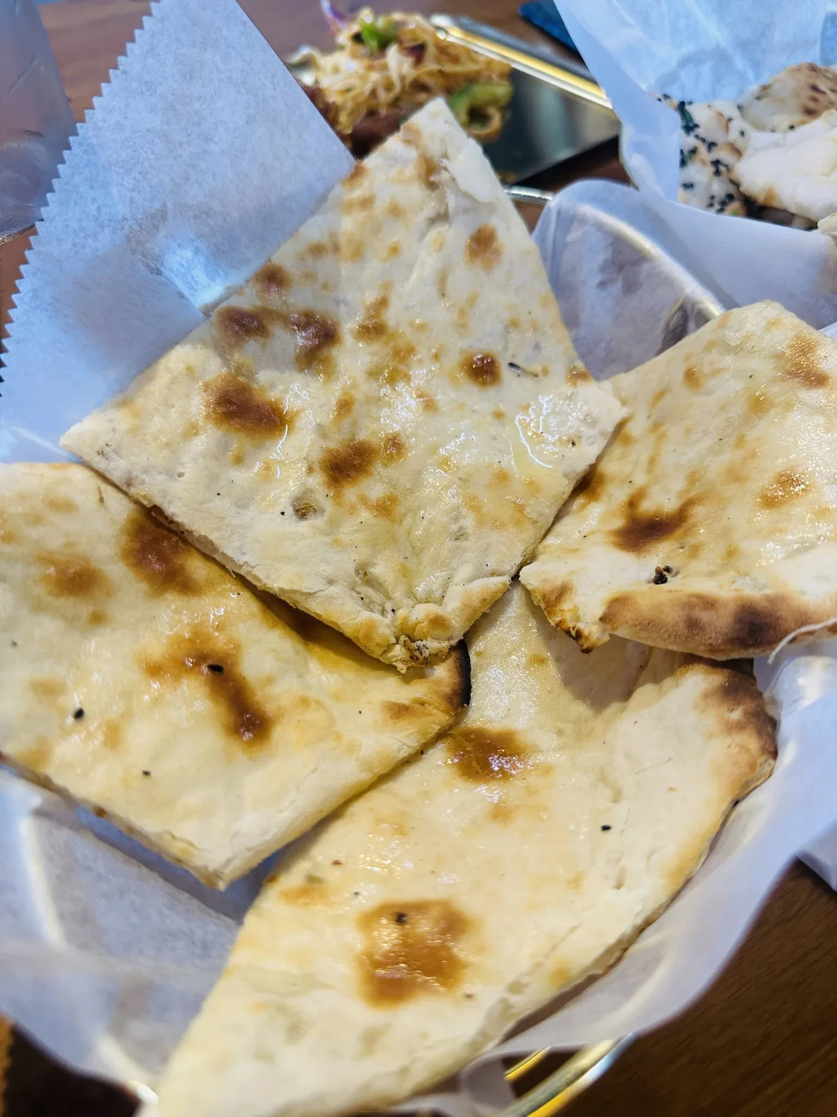 Naan torn into triangles in a paper-lined basket.