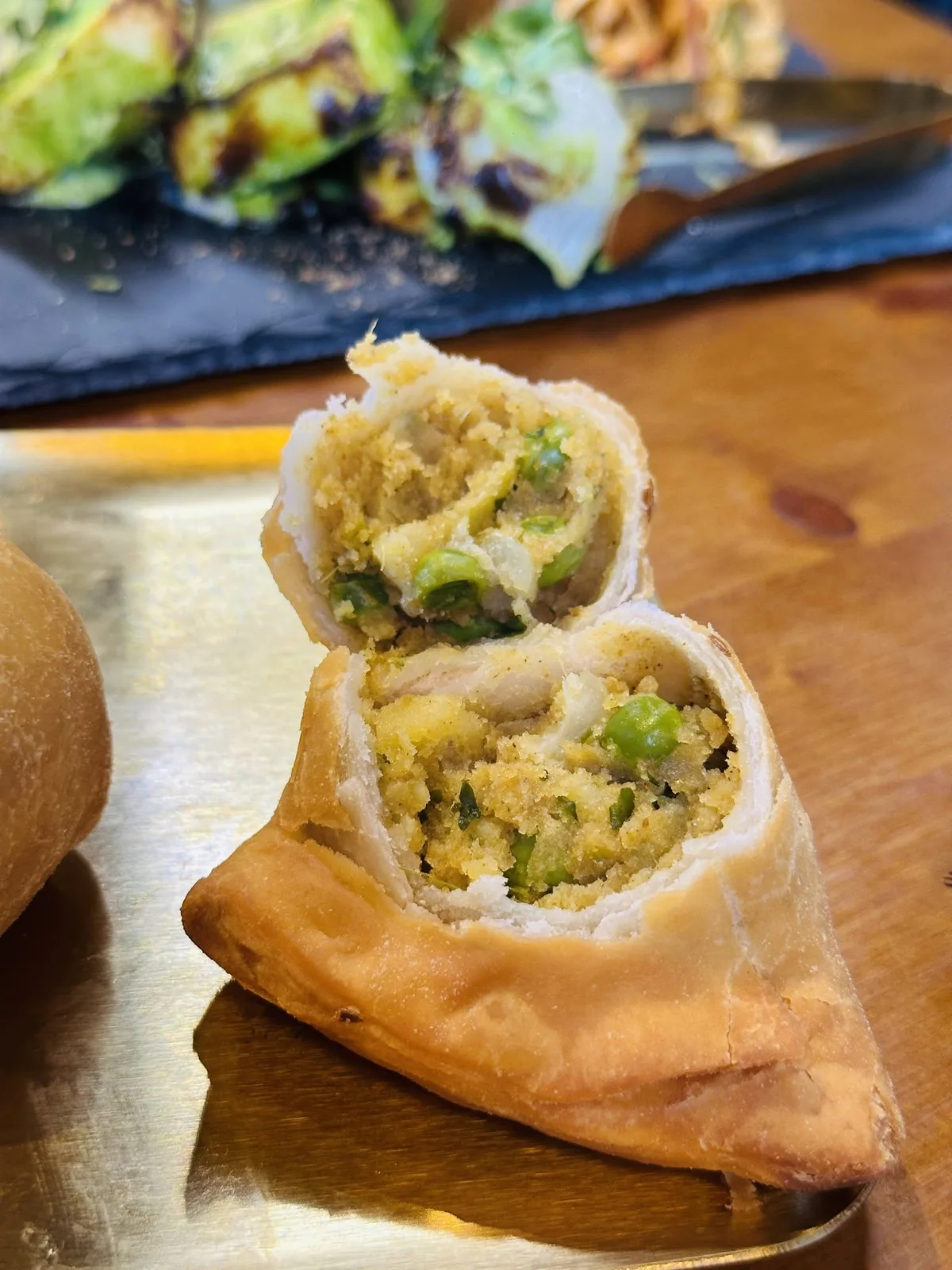 A samosa cut open on a gold tray, its spiced potato and green pea filling showing.