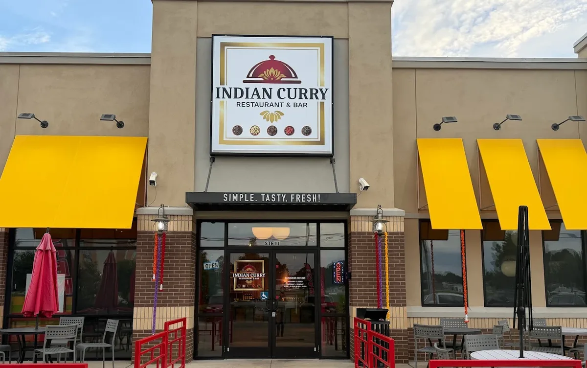 Indian Curry Restaurant & Bar from Montgomery Highway: the lit sign, yellow awnings, marigold garlands on the door pillars and red patio umbrellas.
