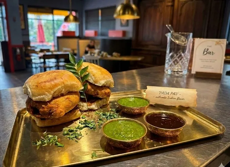Vada pav, the Mumbai street burger, on a board beside a card reading THE Bar.